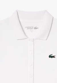 Polo bianco con una vestibilità slim. Presenta un colletto classico, tre bottoni e un accento con il logo di un coccodrillo verde sul petto sinistro.