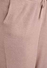 Gaiši rozā ribota auduma ar vertikālu tekstūru, ar sānu kabatām un aukliņu jostas vietā. Materiāls izskatās mīksts un elastīgs.