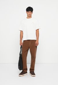 Camiseta blanca de manga corta, pantalones largos a rayas marrones, bolso negro, zapatillas deportivas marrones, diseño sencillo.