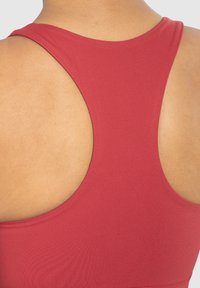 Top rojo sin mangas con diseño de espalda nadadora, fabricado en un tejido liso. Detalles notables incluyen una silueta ajustada y un estilo minimalista.