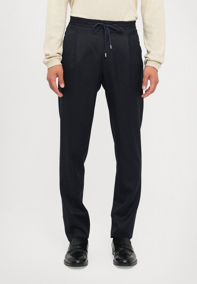 Navy trousers made of lightweight fabric, featuring a drawstring waist, pleats, and side pockets, paired with black shoes.