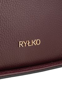 Burgundy tekstureret lædermateriale med et guldtonet "RYŁKO" logo. Har glatte kanter og syninger i detaljerne.