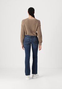Beige knitted sweater with long sleeves, paired with dark blue jeans featuring a classic five-pocket design, and white shoes.