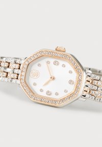 Montre octogonale en argent et or rose avec un cadran blanc, ornée de cristaux autour de la lunette et du bracelet pour un détail supplémentaire.
