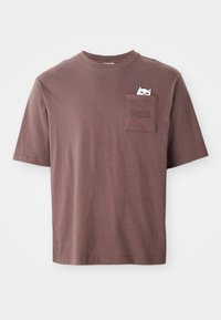 Tricou din bumbac maro cu mâneci scurte. Dispune de un buzunar pe piept cu un grafic al unei pisici care se uită afară și cuvântul "PUMA" embosat pe buzunar.
