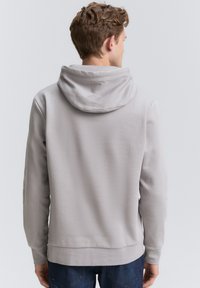 Hoodie gris avec une grande capuche douce, des manches longues et des détails en côtes au niveau de l'ourlet. Texture de tissu lisse, vue de dos, associé à un jean bleu.