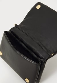 Black leather crossbody bag open showing two compartments and gold magnetic snap closures on a light background.
