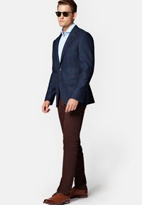 Granatowa marynarka w kratę, jasnoniebieska koszula, brązowe spodnie i brązowe buty. Dodatki obejmują czarne okulary przeciwsłoneczne. Gładki materiał i dopasowany krój.