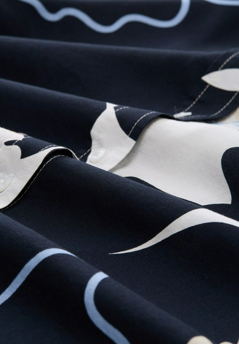 Marineblauer Stoff mit weißen und hellblauen abstrakten Mustern, der klare Falten und sichtbare Nähte aufweist und eine glatte Textur zeigt.