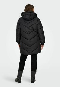 Black padded coat with a chevron quilting pattern, hood, and long sleeves. The coat extends to mid-thigh, paired with black leggings and boots.