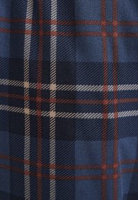 Rutig tyg i mörkblått, med röda och beige linjer. Mjuk textur med ett klassiskt rutmönster, jämnt fördelade fyrkanter och rektanglar.