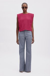 Top sans manches fuchsia avec des plis verticaux, associé à un jean clair évasé avec des coutures latérales contrastantes et une texture lisse.