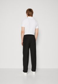 Bílý polo tričko s krátkým rukávem spárované s černými volnějšími kalhotami a bílými teniskami. Kalhoty mají elastický pas a zadní kapsy.