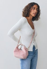 Villane valge kardigan V-kaelusega ja nööpidega, kombineeritud kõrge vöökohaga siniste teksastega. Roosa karvane käekott õlarihmaga.