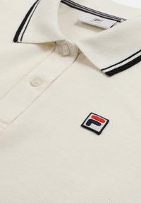 Krämfärgad polo med svart och vit randig krage, texturerad tyg, med en liten broderad logotyp på bröstet.
