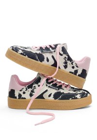 Ζευγάρι sneakers χαμηλού τύπου με ασπρόμαυρο μοτίβο αγελάδας, ανοιχτό ροζ κορδόνια και τακούνι, και λαστιχένιες σόλες σε χρώμα τσίχλας.
