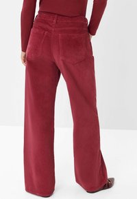 Pantaloni in corduroy a gamba larga di un rosso intenso. Presentano una finitura testurizzata con una vita elastica e due tasche posteriori.