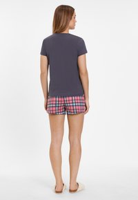 Camiseta de manga corta gris oscuro combinada con pantalones cortos de cuadros rosas que presentan acentos en azul y verde. Tejido suave con un corte relajado.