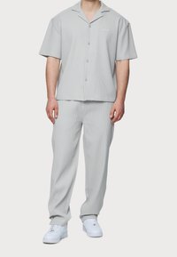 Ljusgrå kortärmad skjorta med krage och knappar, kombinerad med matchande lätta byxor; båda har ett texturerat tyg. Vita sneakers fulländar outfiten.