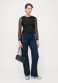Svart langermet topp med gjennomsiktige mesh-ermer, kombinert med mørkeblå slengjeans med sølvøyenlappdetaljer. Tilbehør med en svart håndveske.