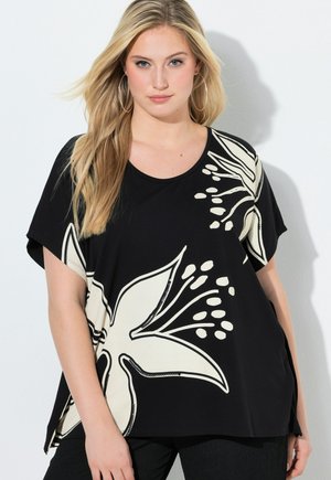 Donna bionda con grandi orecchini a cerchio e una maglia nera larga con una grande stampa floreale bianca sulla parte anteriore e sulle maniche.