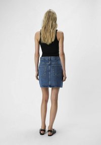 La falda de mezclilla presenta un diseño ajustado con una cintura alta, color azul y bolsillos delanteros y traseros. Está hecha de material de mezclilla clásico.