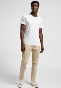 Camiseta blanca de manga corta, pantalones ajustados beige y zapatillas beige. Textura suave; diseño informal con cuello redondo y corte estándar.