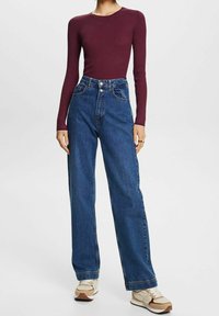 Viininpunainen pitkähihaisen ribbineulospaita yhdistettynä korkeavyötäröisiin leveälahkeisiin sinisiin farkkuihin ja beigeihin tennareihin. Asussa on tavallinen ompelu ja nappikiinnitys.