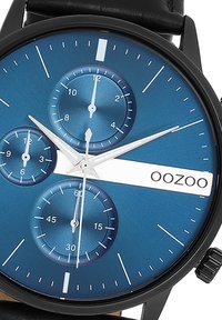 Montre à bracelet en cuir noir avec un cadran bleu, trois sous-cadrans, aiguilles argentées et une barre d'accentuation blanche affichant le nom de la marque "OOZOO."