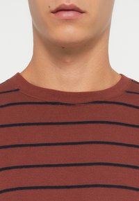 Katoenen T-shirt in verbrande sinaasappel met horizontale marineblauwe strepen, met een ronde halslijn en een zachte textuur. Schoon, eenvoudig ontwerp.