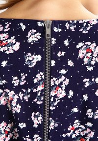 Navy floral dress featuring small pink and white flowers, polka dots, and a visible silver zipper at the back. Soft fabric texture.