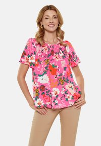 Bluse mit Blumenmuster in leuchtendem Pink, mit gerafftem Ausschnitt, kurzen Ärmeln und lebendigen, bunten Blumenmustern. Weicher Stoff.