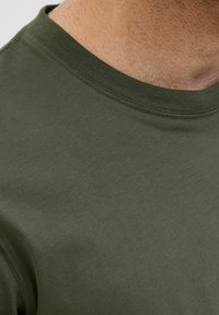 T-shirt verde oliva con collo rotondo, realizzato in morbido cotone; presenta maniche corte e un design semplice e privo di decorazioni.