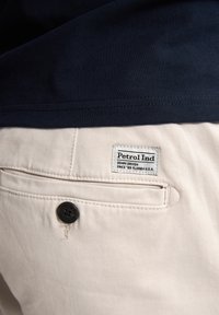 Jasne beżowe spodnie z tylną kieszenią i czarnym guzikiem. Metka głosi: "Petrol Ind, Denim Driven, Since '69 Florida U.S.A." Granatowa koszula na górze.
