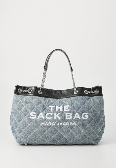 Sac en toile matelassée en denim bleu avec finitions en cuir noir, poignées en chaîne et texte blanc "THE SACK BAG MARC JACOBS" sur le devant.