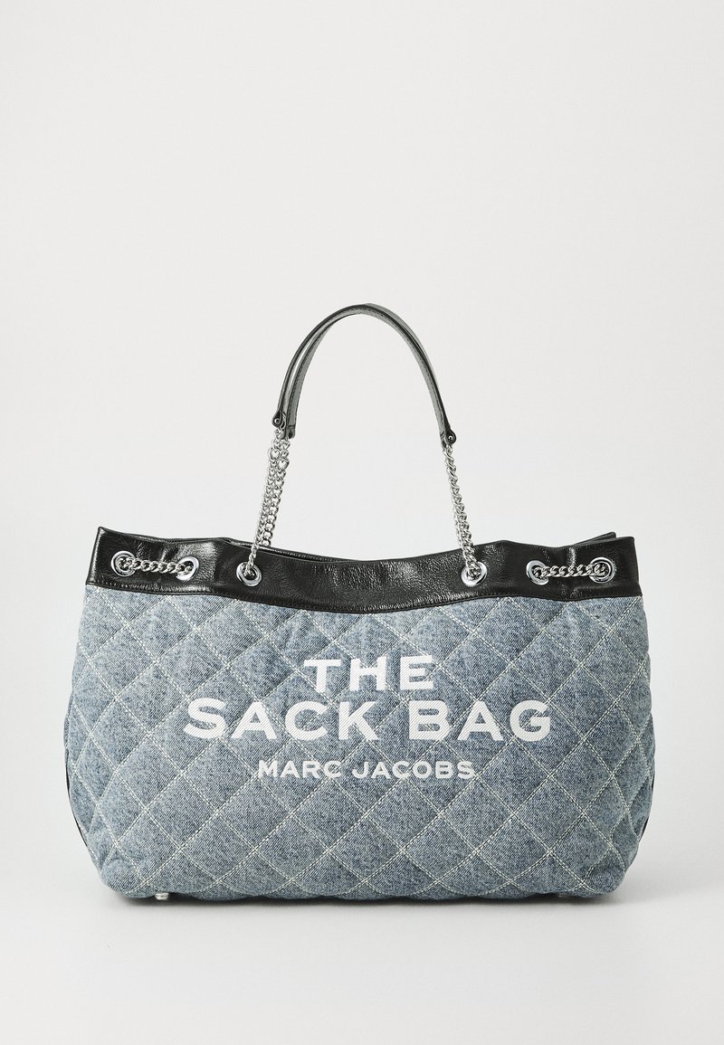 Quilted blue denim tote bag with black leather trim, chain handles, and white text "THE SACK BAG MARC JACOBS" on the front.