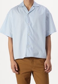 Jasnoniebieska koszula z krótkim rękawem na guziki z pionowymi paskami i kołnierzem typu camp, wykonana z gładkiej tkaniny o luźnym kroju.