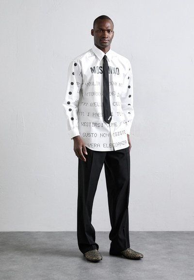 Cămașă albă cu text negru și buline, asortată cu pantaloni negri și pantofi cu model. Prezintă tipografie îndrăzneață și o cravată elegantă.