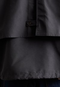 Jachetă ușoară, de culoare gri închis, cu o finisare mată, având închidere cu nasturi și detalii de cusătură vizibile. Textură netedă cu un croi supradimensionat.