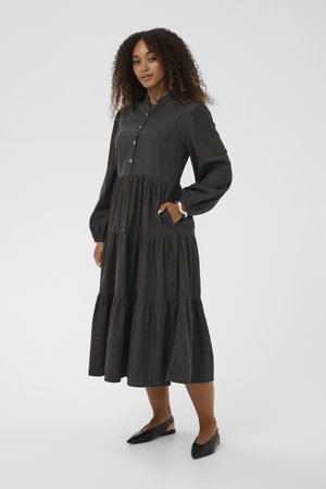 Musthave mustern must tume kihtidega kleit kerge kangaga, millel on pikad puhv-sleeves, nupuvajutus ees ja küljetaskud. Kombineeritud mustade korteritega.