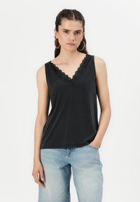 Top nero senza maniche con scollatura a V e rifinitura in pizzo scallop. Tessuto morbido e vestibilità comoda, abbinato a jeans blu chiaro.