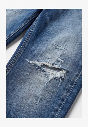 Plave traperice s horizontalnim razderotinom i izblijedjelim nitima na području bedra, prikazujući istrošenu teksturu tkanine i detalje šava.