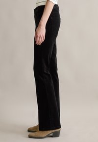 Zwarte corduroybroeken met een recht model. Gecombineerd met beige hakken. Zichtbare achterzak en een lichte textuur in de stof.