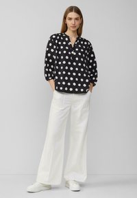 Zwarte shirt met witte stippen, 3/4 mouwen en een V-hals. Gecombineerd met brede witte broeken en witte sneakers. Eenvoudig en modern ontwerp.