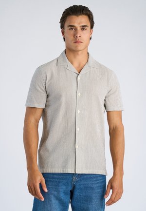 Koszula na krótki rękaw na guziki w jasny, prążkowany wzór, z kołnierzem kampowym, w beżowo-szarych odcieniach, o luźnym kroju, zestawiona z niebieskimi dżinsami.