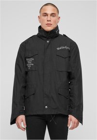 Černá bunda s vysokým límcem, dvěma předními kapsami a vyšitým textem. Tkanina působí hladce, s knoflíkovým zapínáním dole.