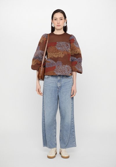 Brun mönstrad tröja med puffärmar, kombinerad med ljusblå vida jeans och beige sneakers; håller en brun axelremsväska.