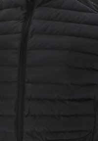 Schwarze Steppweste mit einem gekRachel Stirnband, das horizontale Baffles aufweist, einen durchgehenden Reißverschluss und eine glatte Textur. Keine sichtbare Markenkennzeichnung.
