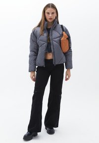 Chaqueta acolchada gris con cuello alto, corte corto, combinada con pantalones cargo negros con grandes bolsillos y un bolso cruzado marrón.