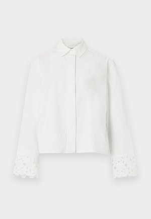 Camicia bianca a maniche lunghe con colletto a punta, patta con bottoni nascosti e polsini decorativi traforati in pizzo sulle maniche.